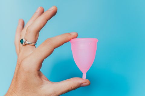 woman holding a pink menstrual cup on blue background