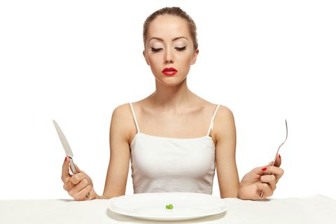 woman holding cutlery and a white plate with a single pea