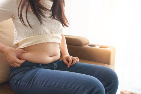 woman holding her own belly when sitting down on sofa in the living room