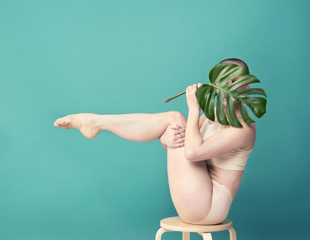 mujer sosteniendo una hoja de monstera en pose de yoga