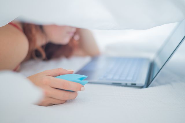 woman holding vibrator while using laptop on bed
