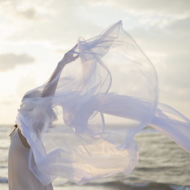 woman holding white sheer fabric on the beach