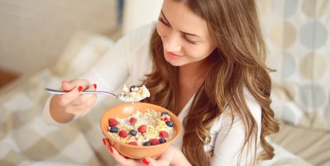 woman in pajamas in bedroom eating muesli with berries