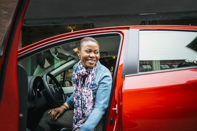 woman in red car smiling with car door open