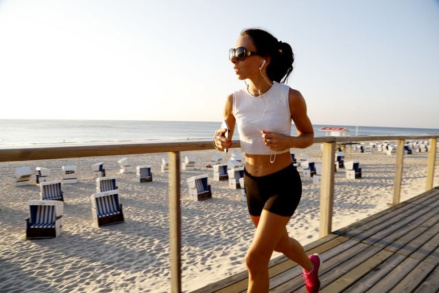 woman jogging on the beach boardwalk while listening to music on smartphone