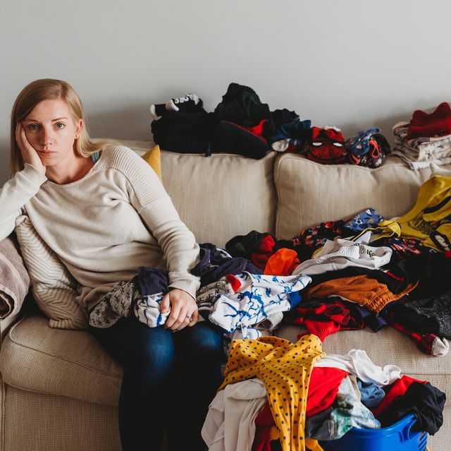A woman looking bored folding large pile of laundry on sofa at home