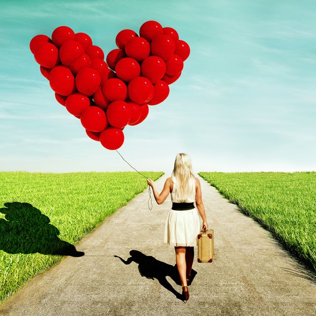 woman looking love while walking with heart shaped red balloons and a suitcase
