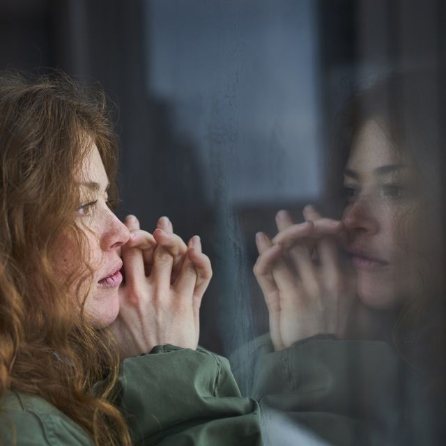 woman looking out of window into her reflection