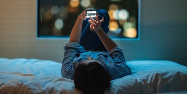 woman lying down on bed and using smart phone at night