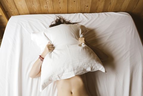 woman lying on bed covering her face with a pillow