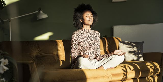 woman meditating while sitting on sofa at home