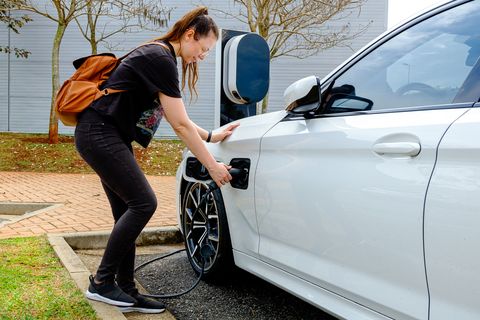 A woman near an electric refueling station carrying her car