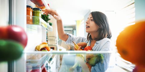 woman picking up some fruits and veggies from the fridge