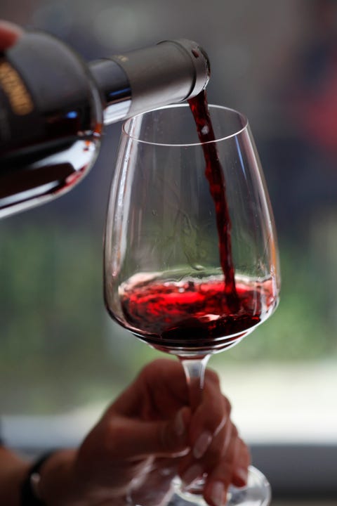 A woman pouring a sampling of red wine at a wine tasting, focus on hands