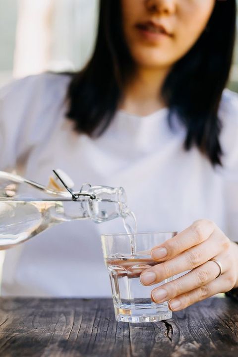 woman pouring water from bottle into glass in outdoor cafe