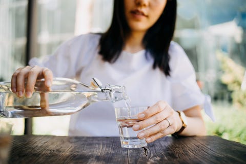 woman pouring water from bottle into the glass at a outdoor cafe