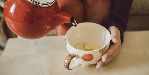 Woman pouring water into tea cup with chopped fresh ginger, close-up