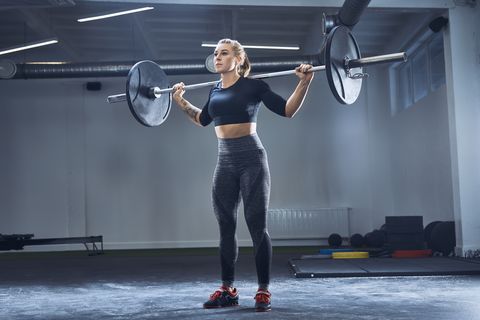 woman practicing barbell squat at gym