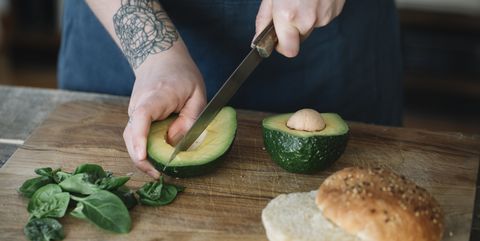 Woman preparing vegan burger, slicing avocado
