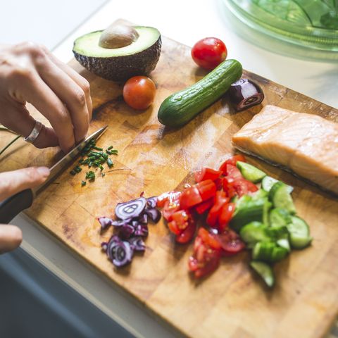 woman preparing vegetables and salmon on chopping board