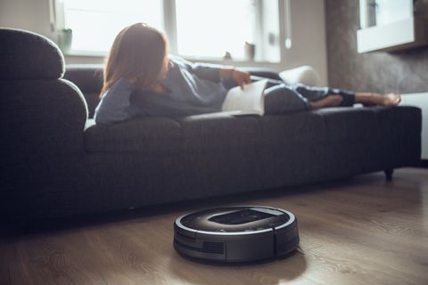 woman reading while robotic vacuum cleaner cleaning house