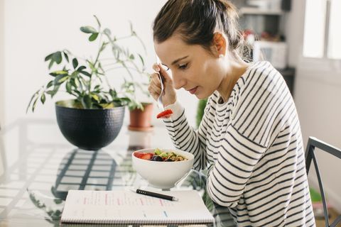 woman sitting at table with fruit muesli looking at notepad