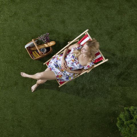 a woman sitting in the sun on a grass in a park with a picnic basket, overhead view