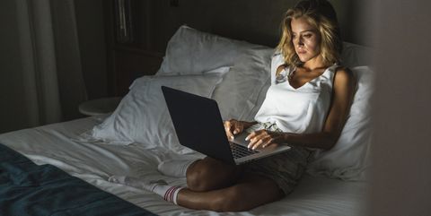Woman sitting on bed, using laptop