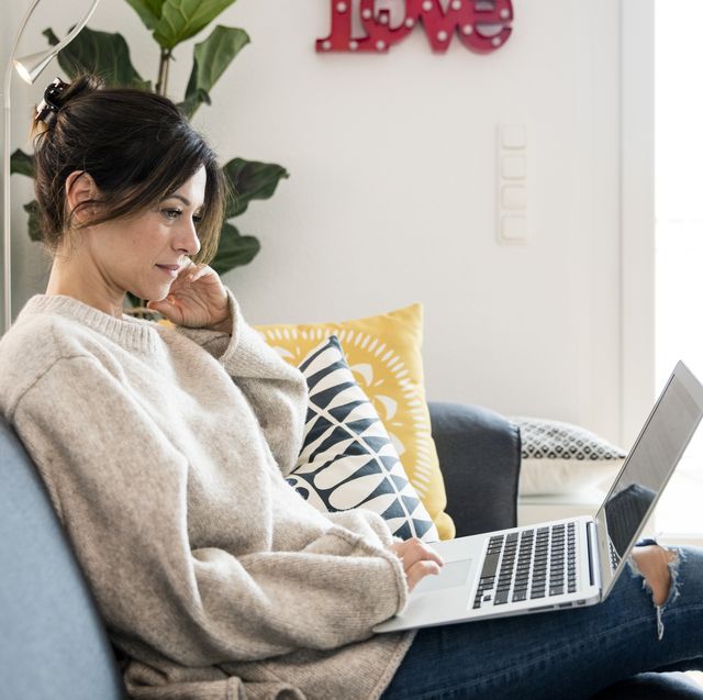 woman sitting on her couch, surfing the net, using laptop