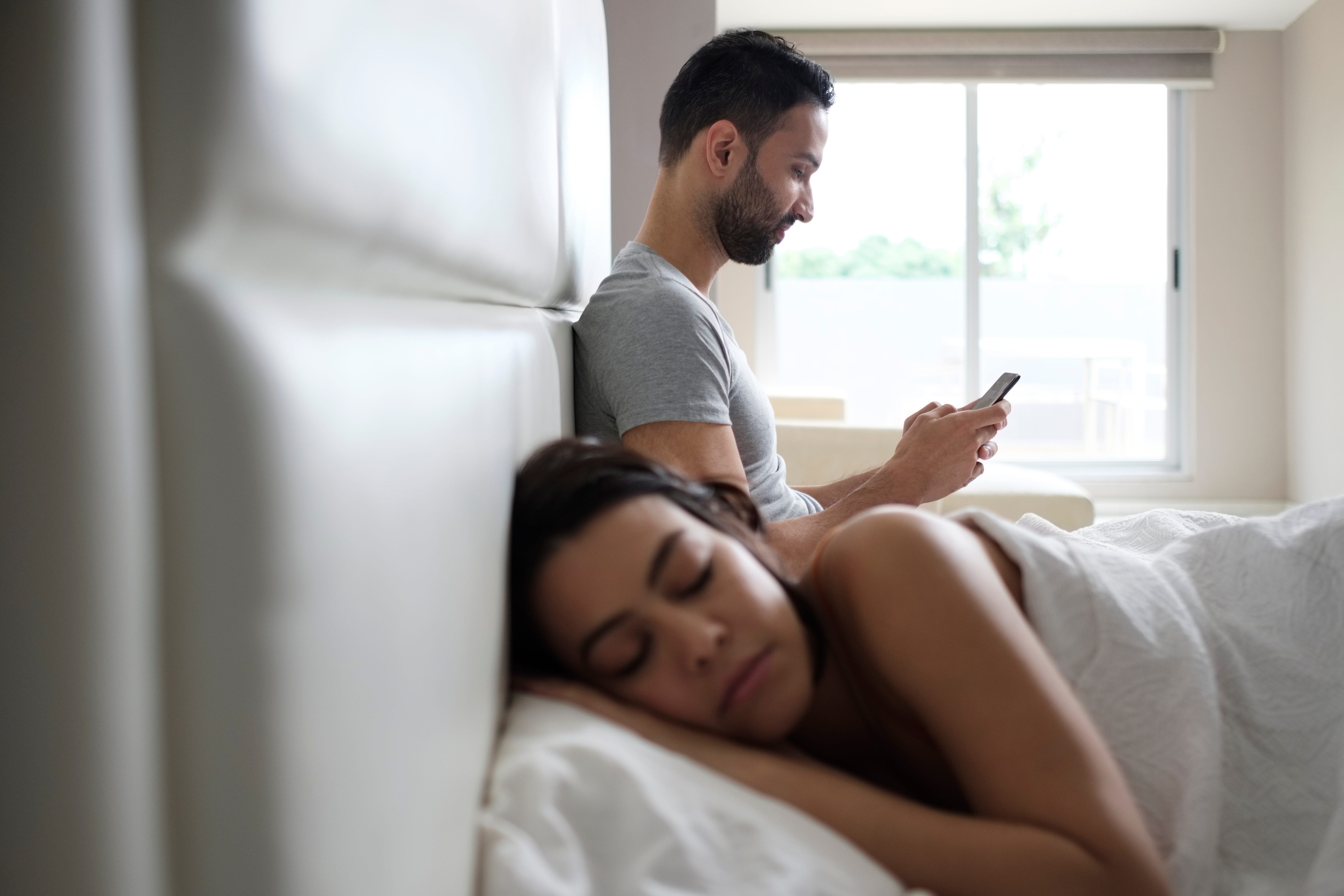 Woman Sleeping While Man Using Smart Phone On Bed At Home woman sleeping while man using smart phone on bed at home