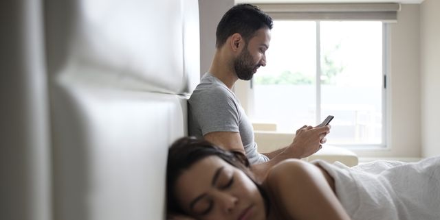 woman sleeping while man using smart phone on bed at home