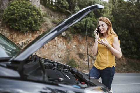 woman talking on cell phone for roadside assistance while standing in car