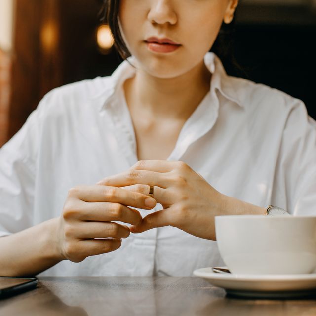 woman touching the wedding ring on her finger nervously while having coffee and waiting in cafe