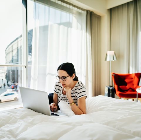Woman Using Laptop On A Bed In Hotel Room