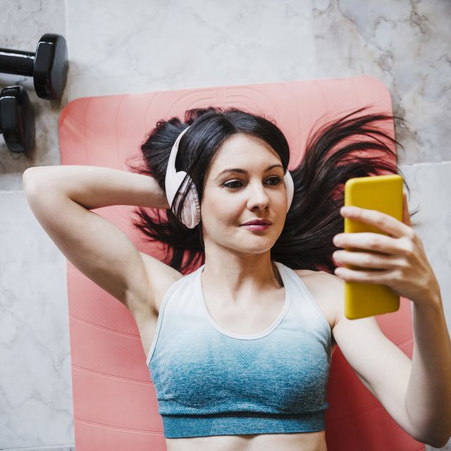 woman using smart phone while relaxing on exercise mat at home