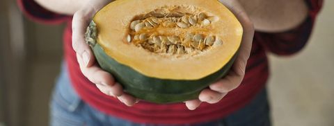 A woman wearing a red striped shirt holds out half of an organic acorn squash in her kitchen in Seattle, Washington.