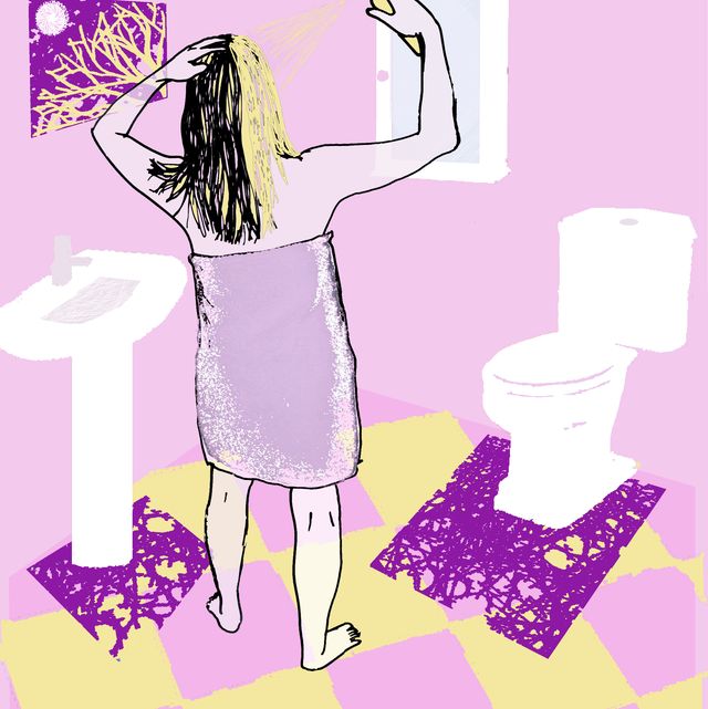 A woman wearing a towel in the bathroom while spraying her hair