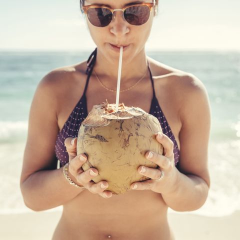 Woman wearing sunglasses and bikini while drinking coconut water at beach against sea