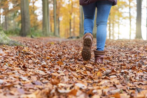 woman with boots walking on autumn leaves in forest