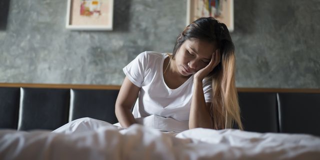 Woman With Headache Sitting On Bed At Home
