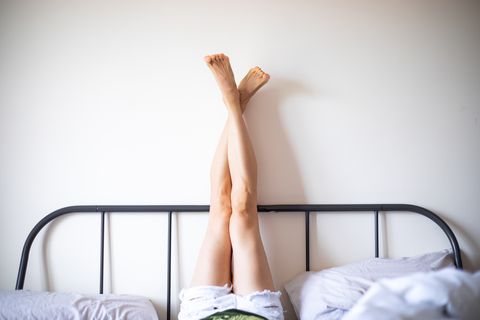 woman with legs raised wearing white shorts lying on bed