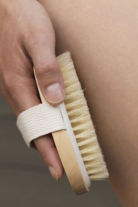 Woman's arm holding dry brush to top of her leg. Cellulite treatment, dry brushing