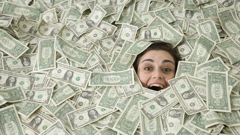 een gelukkige vrouw ligt onder een stapel dollarbiljetten