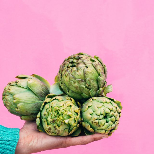 hand holding four artichokes on a pink background