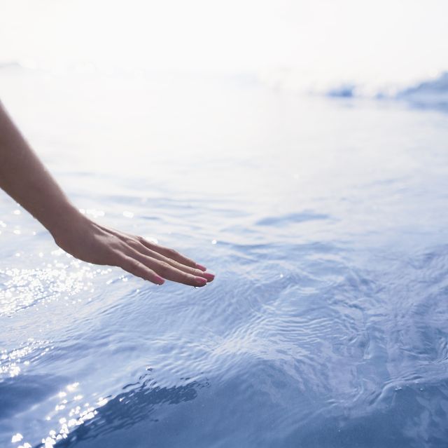 woman's hand reaching to touch the ocean
