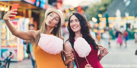 Women at the amusement park eating pink cotton candy and taking selfie/vlogging