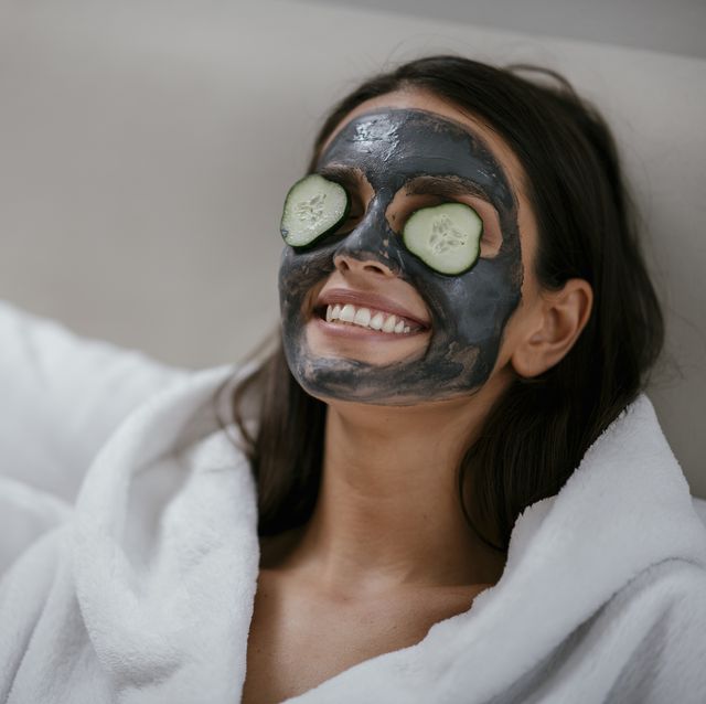 Mujer con mascarilla facial negra y rodajas de pepino en los ojos.