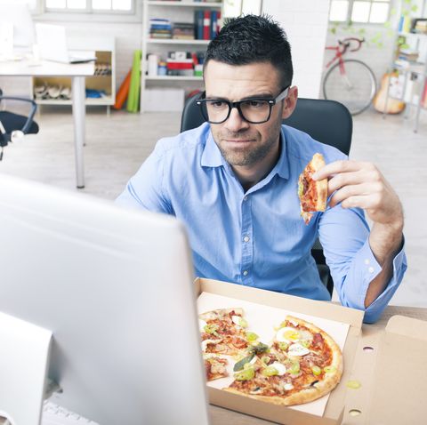 Worried businessman eating pizza at the office