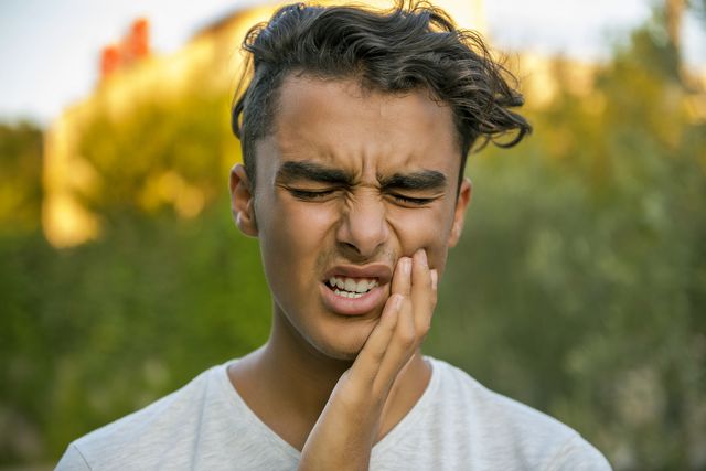 worried teenage boy rubbing his mouth because of toothache