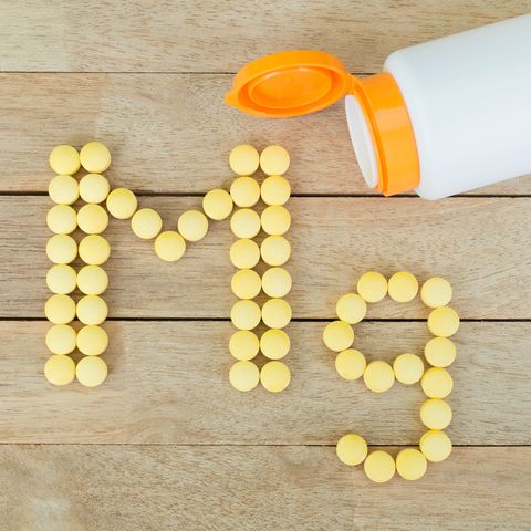 Yellow pills forming shape to Mg alphabet on wood background